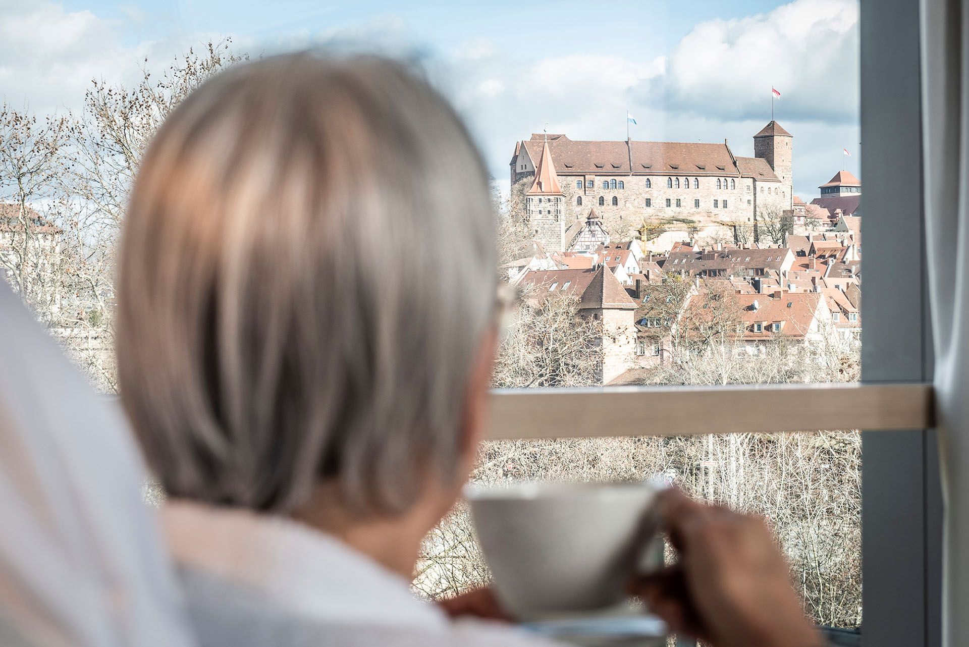 Ein Patient liegt im Krankenbett, trinkt einen Tee und schaut aus dem Fenster direkt auf die Nürnberger Kaiserburg.